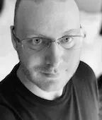 Black‑and‑white portrait of a person wearing glasses, looking directly at the camera.