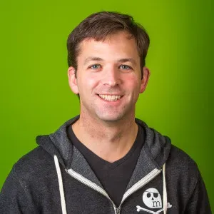 Portrait of Ryan, one of the founders of MetaGeek, standing in front of a bright green background and smiling while wearing a dark hoodie with a skull‑and‑crossbones logo.